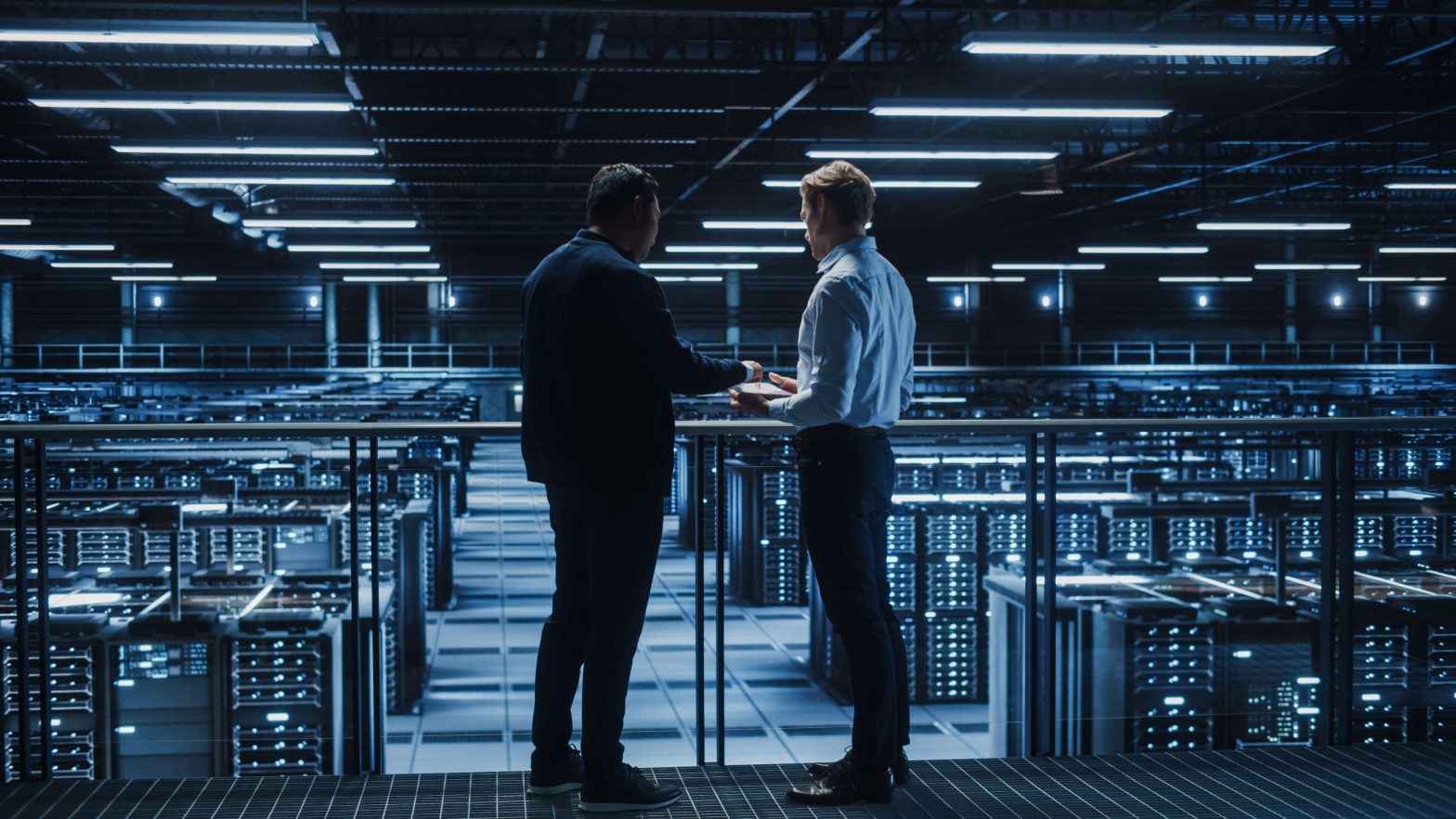 Two IT professionals discussing infrastructure operations inside a modern data center with rows of servers in the background.